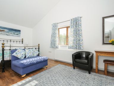 A bedroom with a metal bed frame a blue loveseat with patterned cushions a black armchair wooden desk and floral curtains at Lambley View in Bude