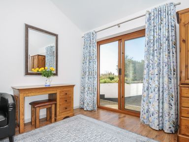 A room with a wooden desk and stool a mirror floral curtains and a glass door leading outside at Lambley View in Bude