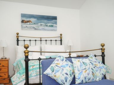 A bedroom with a metal bed frame a wooden nightstand two lamps and a blue sofa with patterned pillows at Lambley View in Bude