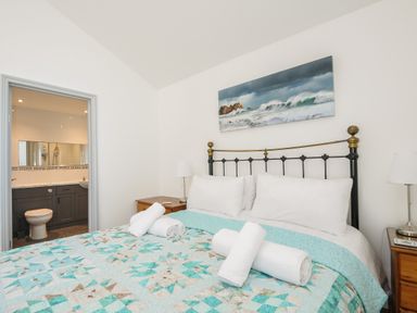 A bedroom with a bed with a quilt and towels a metal headboard bedside tables with lamps and an adjacent bathroom at Lambley View in Bude