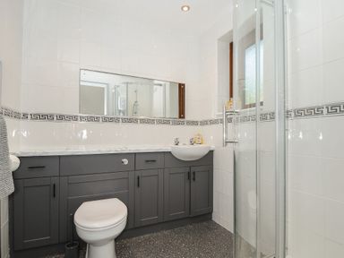 A bathroom with a toilet sink cabinets large mirror window and glass shower at Lambley View in Bude