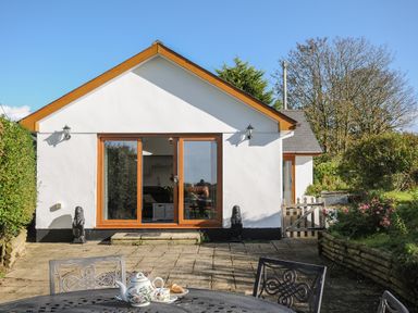 A patio with metal table and chairs and a teapot set in front of a white building with sliding glass doors at Lambley View in Bude