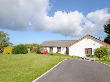 A single story house with a driveway and garden with shrubs under a blue sky at Lambley View in Bude