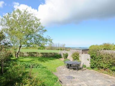 A garden with a tree, lawn, patio area with a table and chairs, and a wooden fence at Lambley View in Bude
