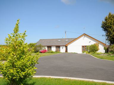 A single-story house with a sloped roof and driveway surrounded by grass and bushes at Lambley View in Bude