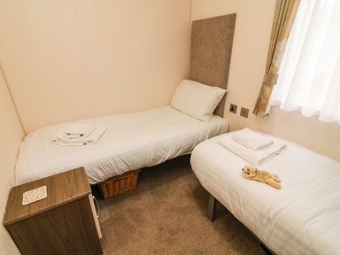 A small bedroom with two single beds with white bedding a wooden nightstand and a window with curtains at 3 Yealands Carnforth