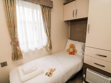 A single bed with stuffed animals and folded towels next to a window with curtains in a bedroom at 3 Yealands in Carnforth