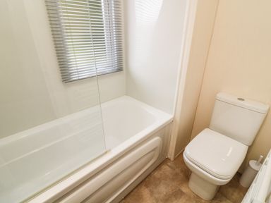 A bathroom with a bathtub next to a toilet and a window with blinds at 3 Yealands in Carnforth