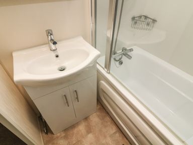 A bathroom with a white sink cabinet and a bathtub with a shower attachment at 3 Yealands in Carnforth