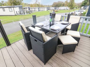 An outdoor dining area with a black wicker table and chairs on a wooden deck at 3 Yealands in Carnforth