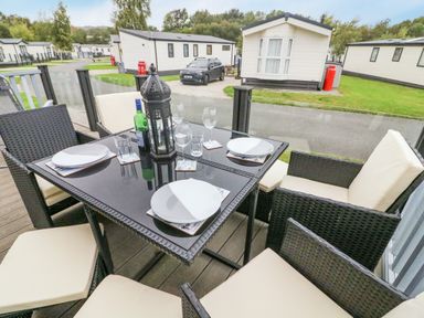 An outdoor dining table with chairs set with plates and glasses on a deck with mobile homes and a car in the background at 3 Yealands in Carnforth