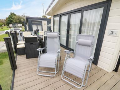 A deck with two reclining chairs and a dining table with wicker chairs at 3 Yealands in Carnforth