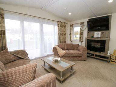 A living room with two brown sofas a coffee table a mounted TV and fireplace at 3 Yealands in Carnforth
