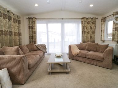 A living room with two brown sofas, a wooden coffee table, and floral curtains at 3 Yealands in Carnforth