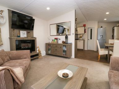 A living room with two brown sofas a wooden coffee table a cabinet with a mirror and a mounted television at 3 Yealands in Carnforth