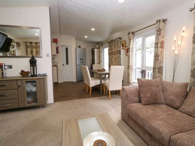 A living room with a brown sofa and a dining area with white chairs and a wooden table at 3 Yealands in Carnforth