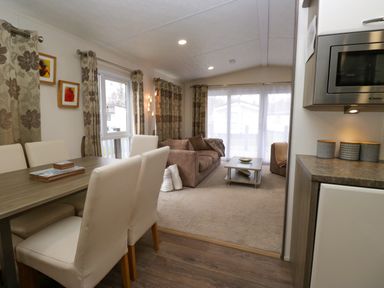 A dining area with six chairs and a table next to a living room with two sofas and a coffee table at 3 Yealands in Carnforth