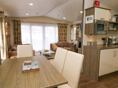 A dining table with chairs in an open living area with sofas kitchen cabinets and a microwave at 3 Yealands in Carnforth