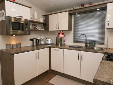 A kitchen with cabinets microwave toaster kettle and double sink with blinds at 3 Yealands in Carnforth