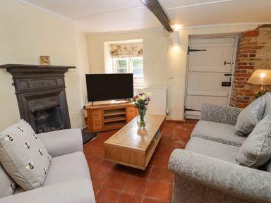 A living room with two sofas a wooden coffee table with flowers a television on a wooden stand a fireplace and a door at 5 Packhorse in Purton