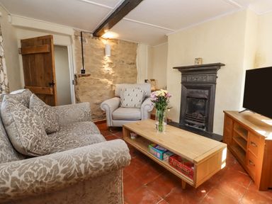 A living room with patterned sofa armchair wooden coffee table with flowers and board games fireplace and television at 5 Packhorse in Purton