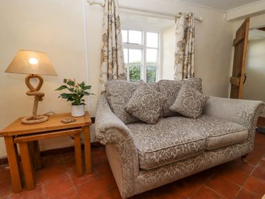 A living room with a patterned sofa with cushions next to a wooden table with a lamp and a potted plant at 5 Packhorse in Purton