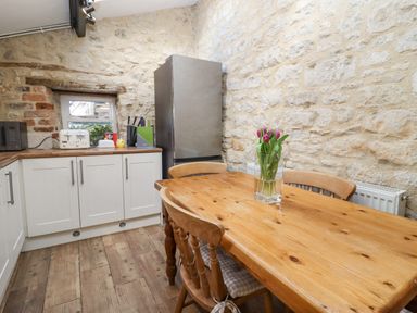 A kitchen with a wooden table and chairs and pink flowers on the table at 5 Packhorse in Purton