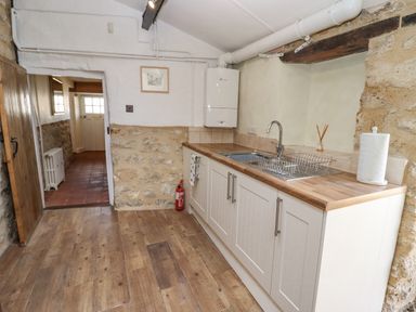 A kitchen with a wooden countertop sink and cabinets and an open door leading to a hallway at 5 Packhorse in Purton
