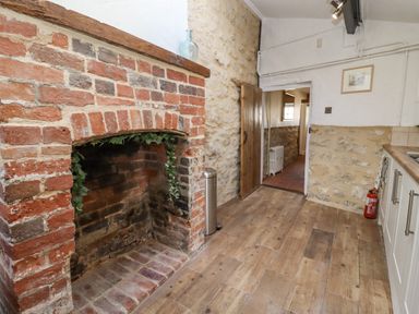 A kitchen with a brick fireplace stone walls wooden floor and a fire extinguisher at 5 Packhorse in Purton