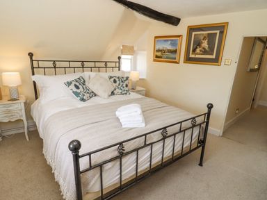A bedroom with a metal bed frame two bedside tables with lamps wall paintings and folded towels on the bed at 5 Packhorse in Purton