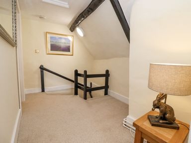 A staircase landing area with beige carpet a wooden side table with a rabbit lamp and a framed picture on the wall at 5 Packhorse in Purton