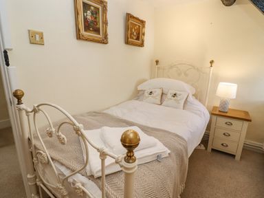 A bedroom with a single white metal bed with gold accents two pillows with bees a bedside table with a lamp and two paintings on the wall at 5 Packhorse in Purton