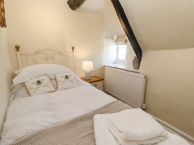 A bedroom with a white metal bed frame, two bee cushions, a bedside table with a lamp, and a window with a ceramic vase at 5 Packhorse in Purton