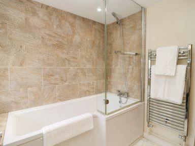 A bathroom with a bathtub and shower next to a towel rack with white towels at 5 Packhorse in Purton