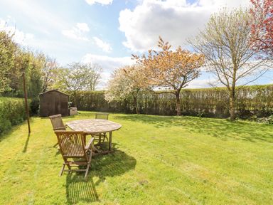 A garden with a wooden table and chairs a shed and trees at 5 Packhorse in Purton