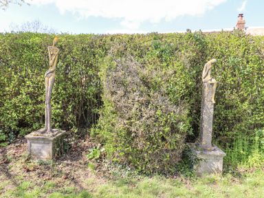 Two tall sculptures on stone pedestals in front of a hedge with grass and plants at 5 Packhorse in Purton