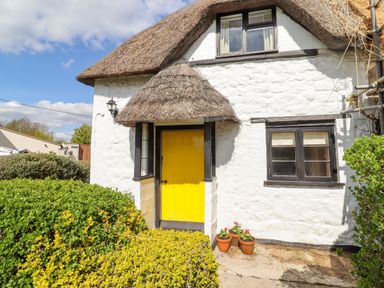 A cottage with a thatched roof yellow door and potted plants outside at 5 Packhorse in Purton