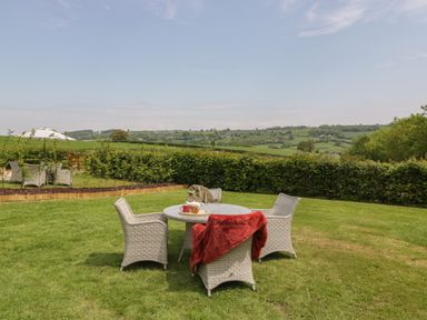 An outdoor seating area with a round table and four chairs on grass with a red blanket and cups at The Hayloft in Stockland Honiton