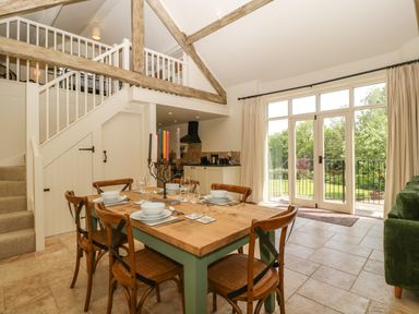 A dining area with a wooden table set for six next to large glass doors and a staircase with an open loft at The Hayloft in Stockland Honiton