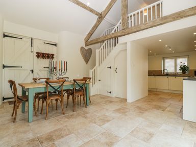 A dining area with a wooden table and chairs next to a staircase in an open kitchen space at The Hayloft in Stockland Honiton