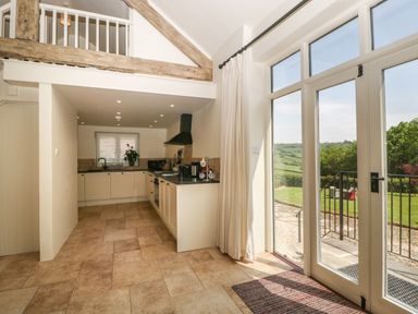 A kitchen with white cabinets and black countertops next to glass doors overlooking a garden at The Hayloft in Stockland Honiton