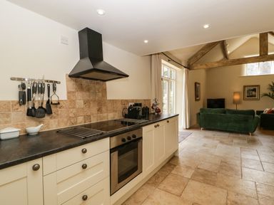 A kitchen with cream cabinets black countertop stove and oven next to a living area with green sofas and wooden beams at The Hayloft in Stockland Honiton