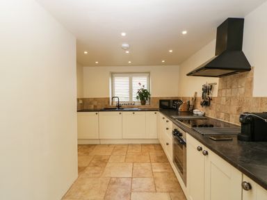 A kitchen with cream cabinets a black countertop and tiled floor at The Hayloft in Stockland Honiton