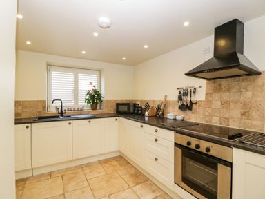 A kitchen with white cabinets black countertop built-in oven stovetop microwave and a window with shutters at The Hayloft in Stockland Honiton