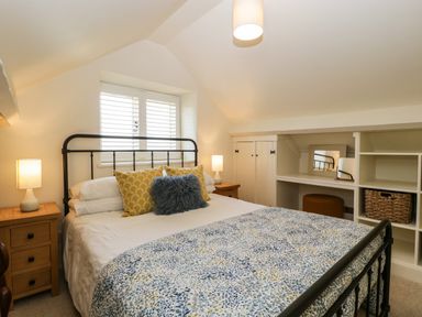 A bedroom with a double bed with pillows and a patterned bedspread two bedside tables with lamps a window with shutters and built in shelving at The Hayloft in Stockland Honiton