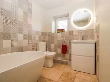 A bathroom with a freestanding bathtub toilet sink with boiler and a round illuminated mirror at The Hayloft in Stockland Honiton