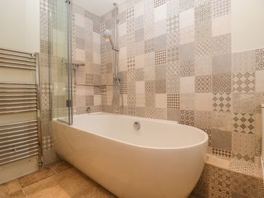 A bathroom with a bathtub a shower head patterned tiles on the wall and a heated towel rail at The Hayloft in Stockland Honiton