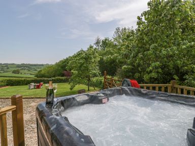 An outdoor hot tub with bubbling water and champagne glasses next to countryside views at The Hayloft in Stockland Honiton