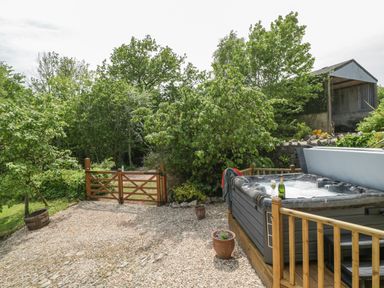 An outdoor area with a hot tub wooden gate trees and a gravel ground at The Hayloft in Stockland Honiton