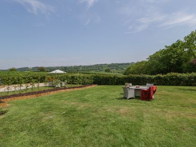 A grassy garden with outdoor dining furniture and an umbrella in the background at The Hayloft in Stockland Honiton
